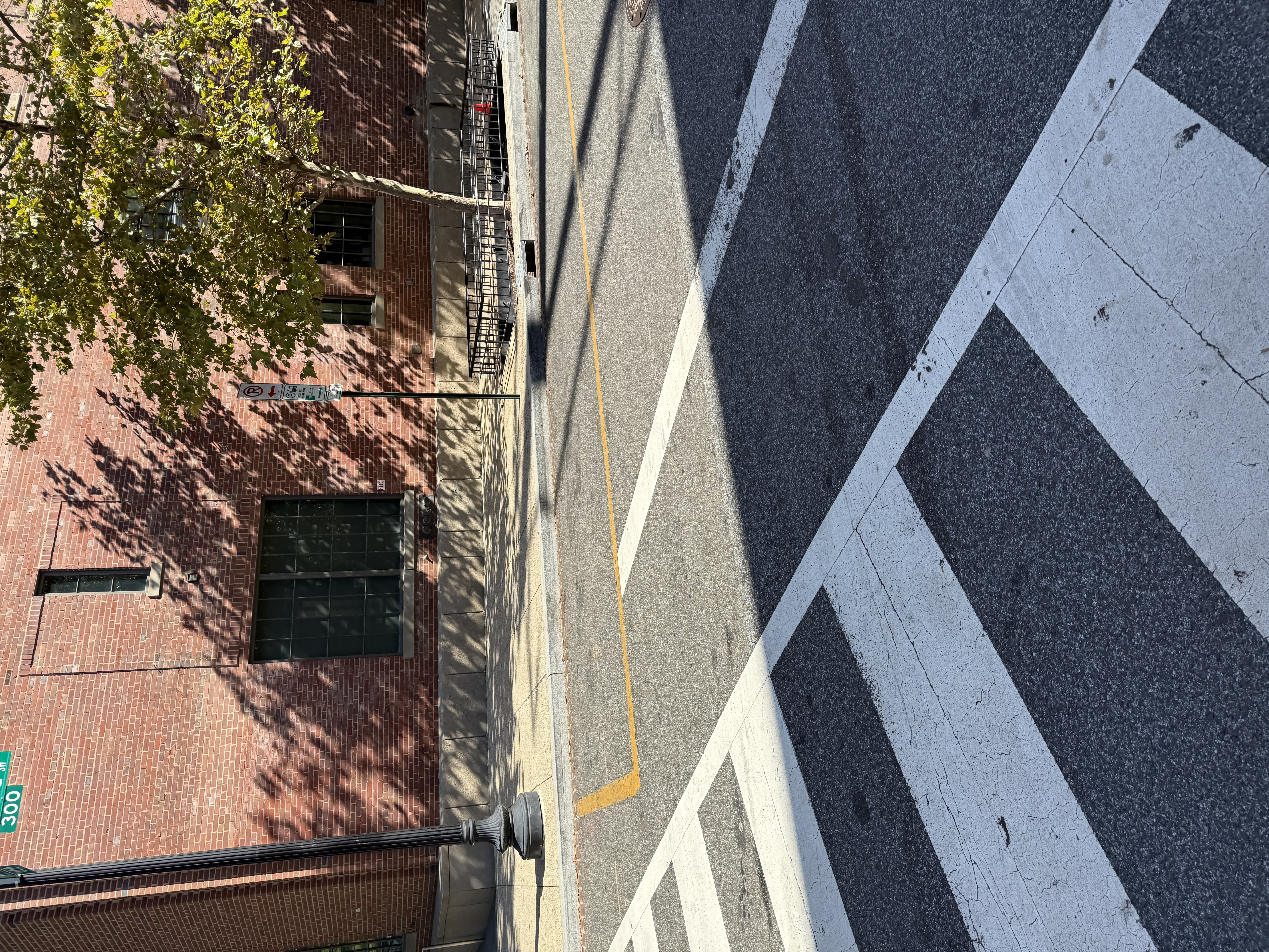Photo 2 of 2: Same DDOT-permitted daylighting failure on the Museum of the Bible block of 4th St SW, documented twice. Frame 1 (Apr 2026): a tour bus parked exactly where the yellow paint permits, with a passenger vehicle stopped inside the crosswalk markings beside it -- the consequence. Frame 2 (Oct 2025): empty curb shows the paint extending right to the crosswalk with no setback -- the cause.
