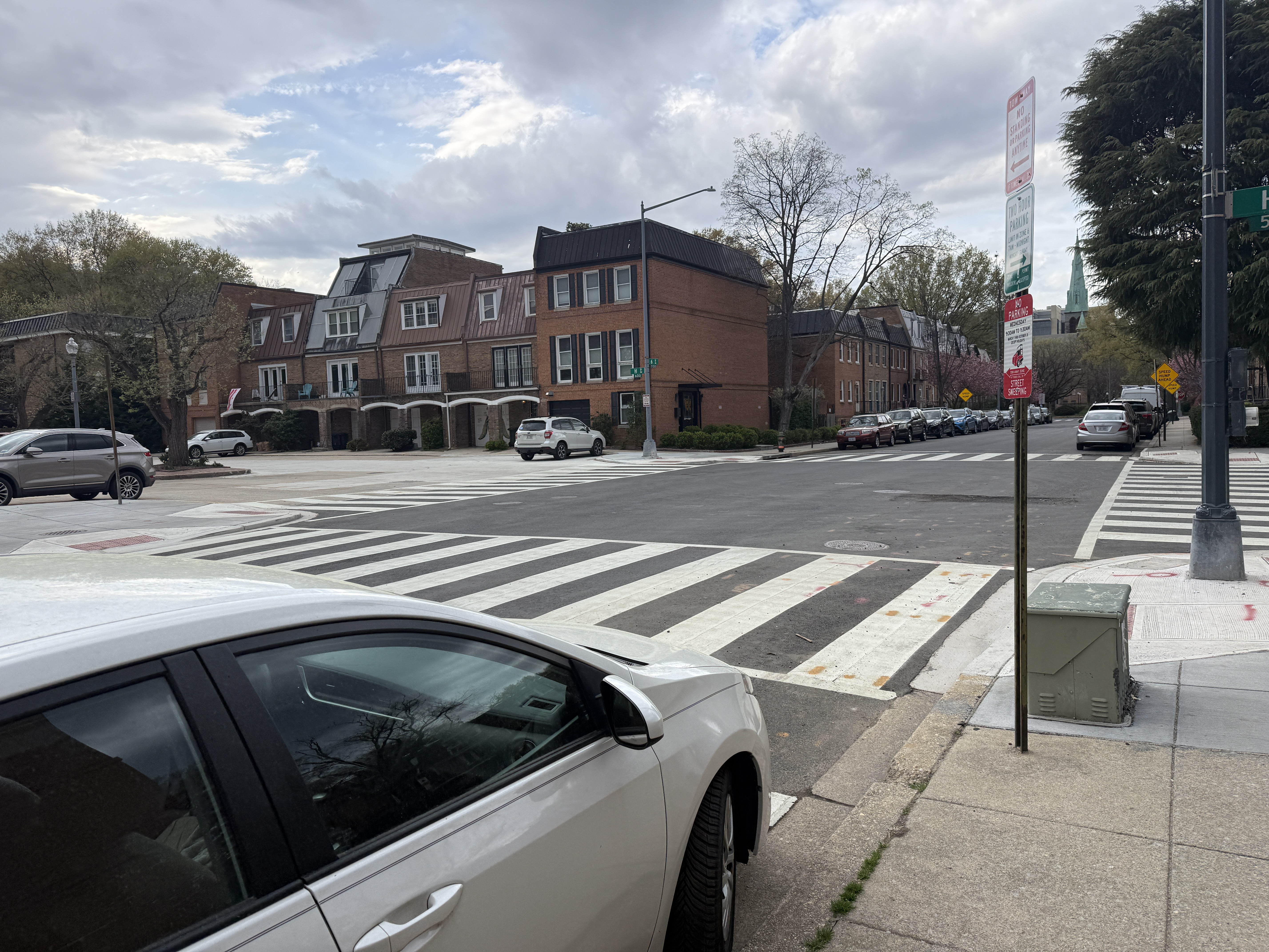 Parking sign at 6th and K Street SW authorizes parking within the daylighting zone of the crosswalk. A white sedan is parked in the zone exactly as the sign allows. The violation is in the signage itself, not the driver's behavior.