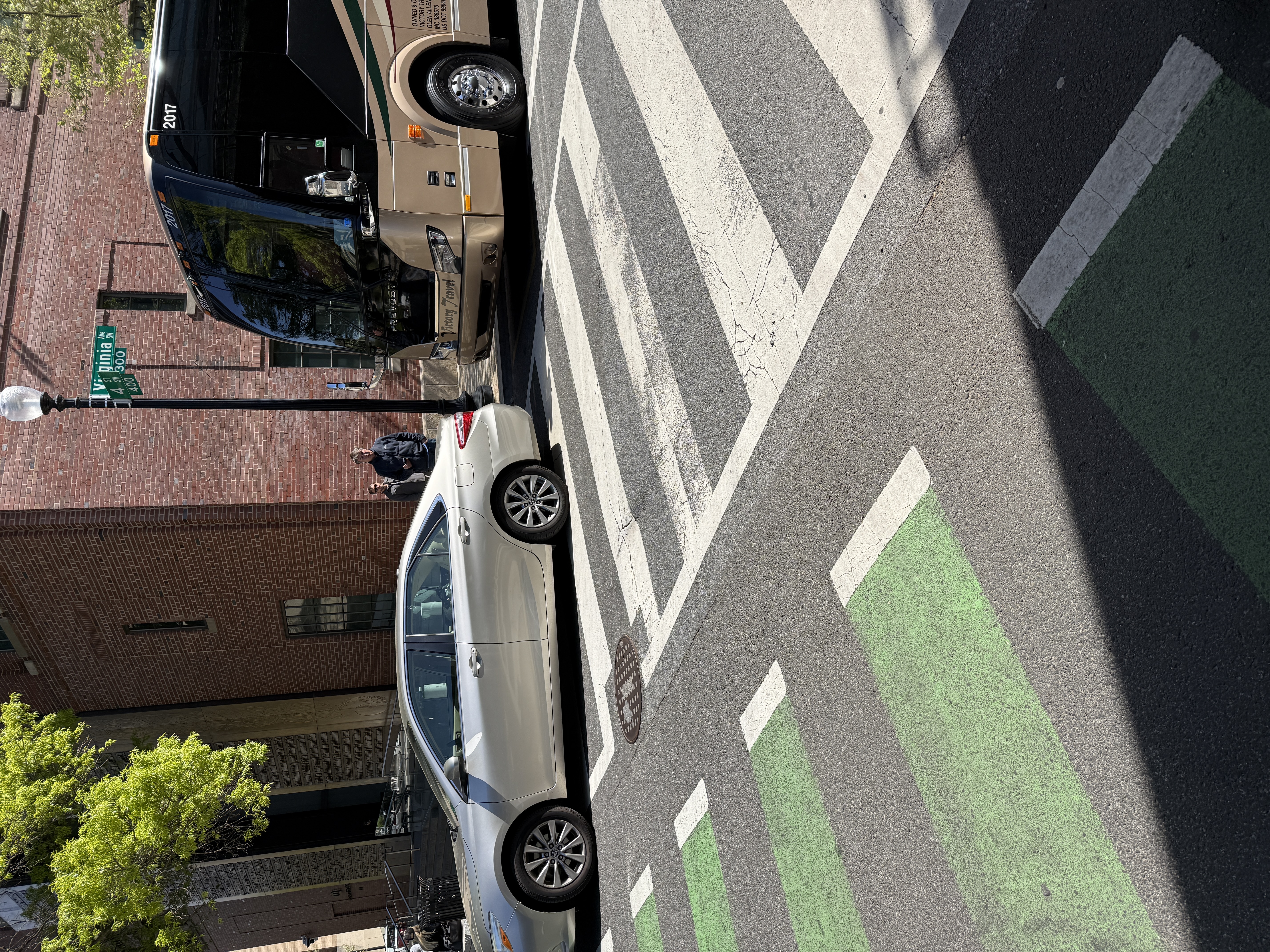 Same DDOT-permitted daylighting failure on the Museum of the Bible block of 4th St SW, documented twice. Frame 1 (Apr 2026): a tour bus parked exactly where the yellow paint permits, with a passenger vehicle stopped inside the crosswalk markings beside it -- the consequence. Frame 2 (Oct 2025): empty curb shows the paint extending right to the crosswalk with no setback -- the cause.