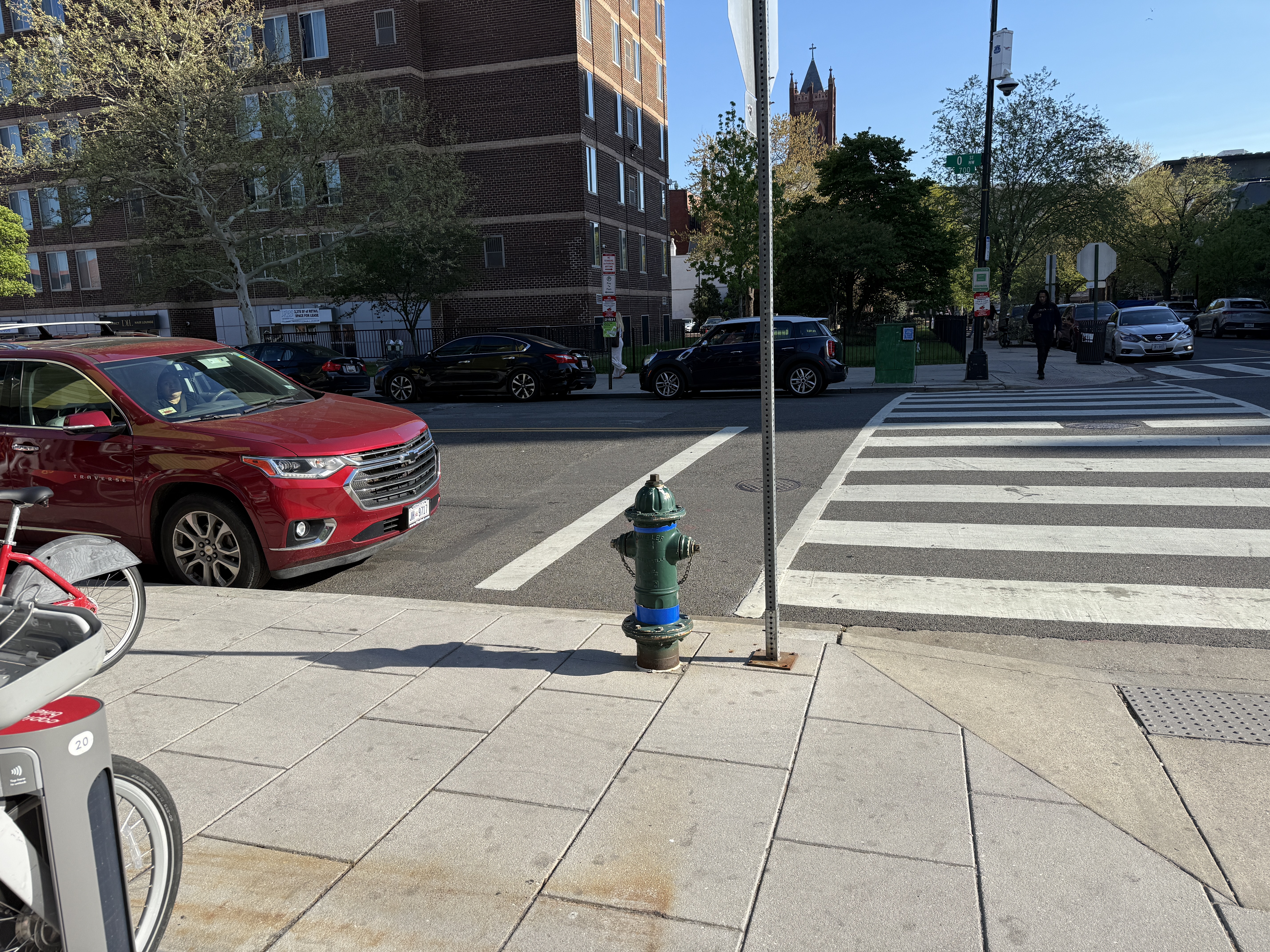 Red Chevy Traverse parked right up against the crosswalk on the 700 block of O St NW. A fire hydrant and Capital Bikeshare station sit at the corner, but no bollard, curb extension, or daylighting marking keeps vehicles back from the crossing.