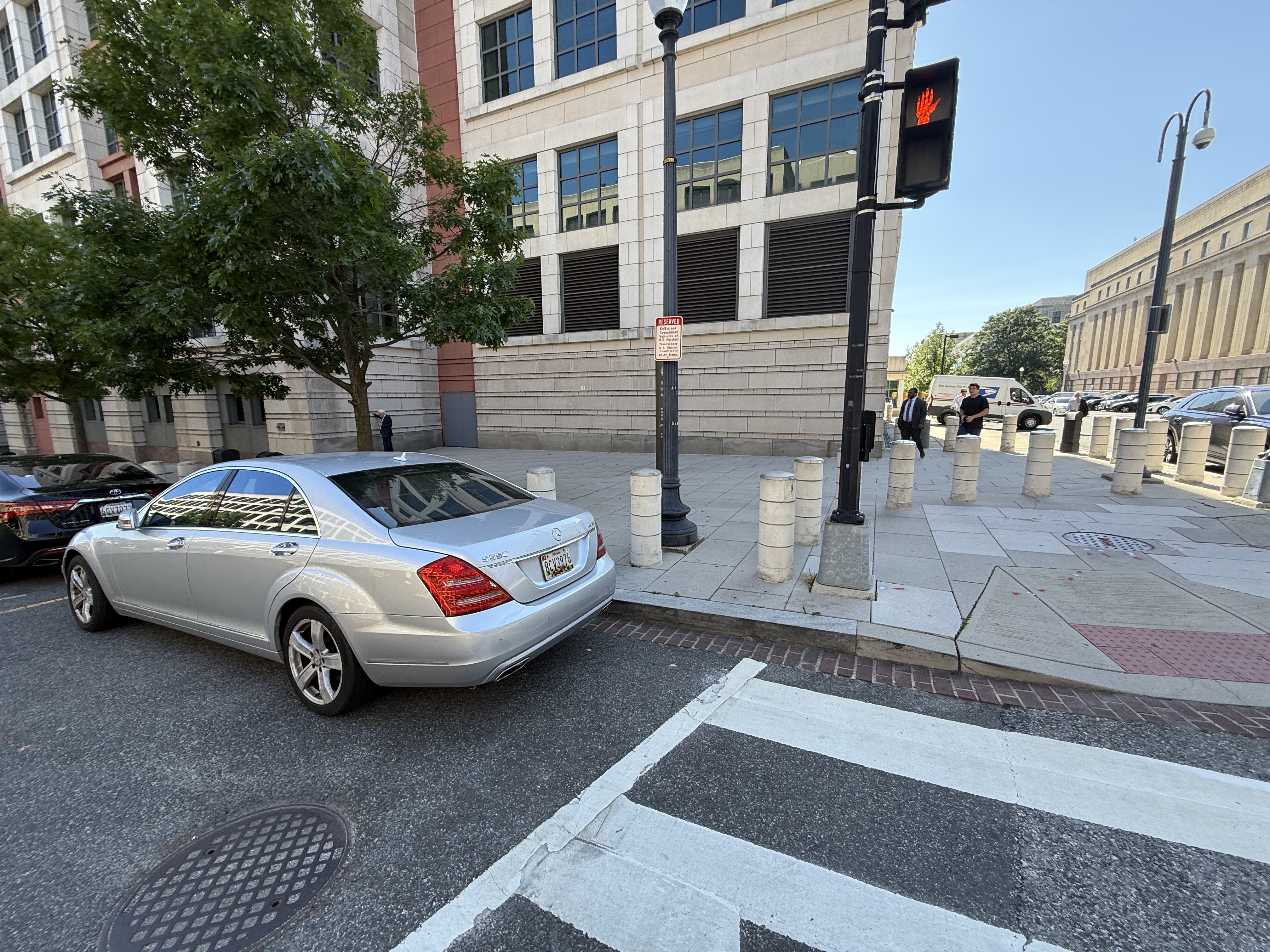 Photo 2 of 2: A private Maryland-tagged Mercedes S550 (MD plate 8CV3976) parked against the marked crosswalk at the corner of 333 Constitution Avenue NW and 3rd Street NW, beside a U.S. Marshals Reserved -- Official Government Vehicles At All Times sign that authorizes parking right up to the crosswalk at the federal courthouse.